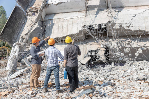 trois personnes devant un bâtiment détruit après un séisme