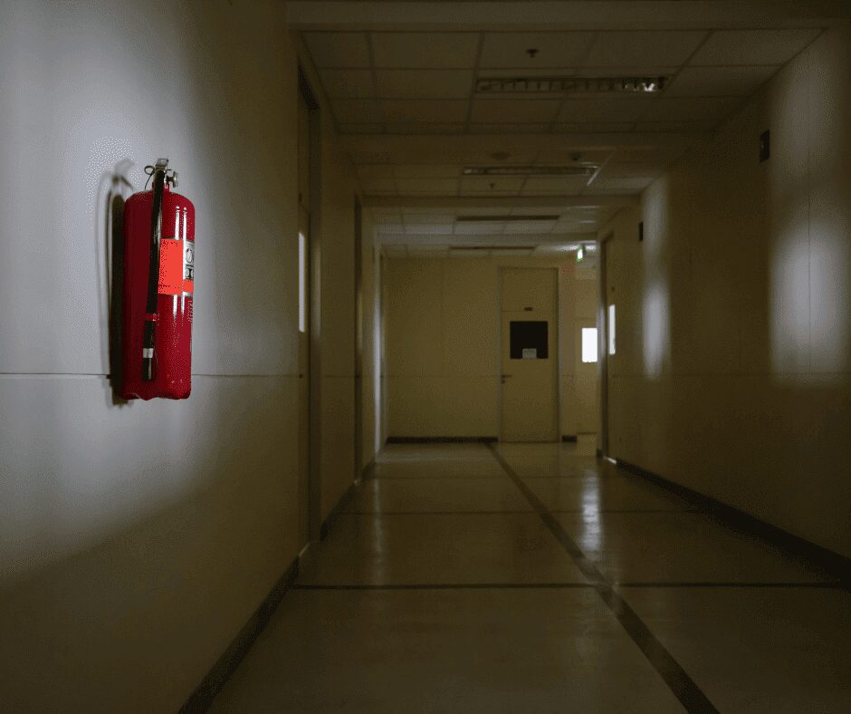 Extincteur rouge monté sur un mur dans un couloir vide, illustrant les mesures de sécurité incendie avec un électroaimant pour le maintien des portes coupe-feu